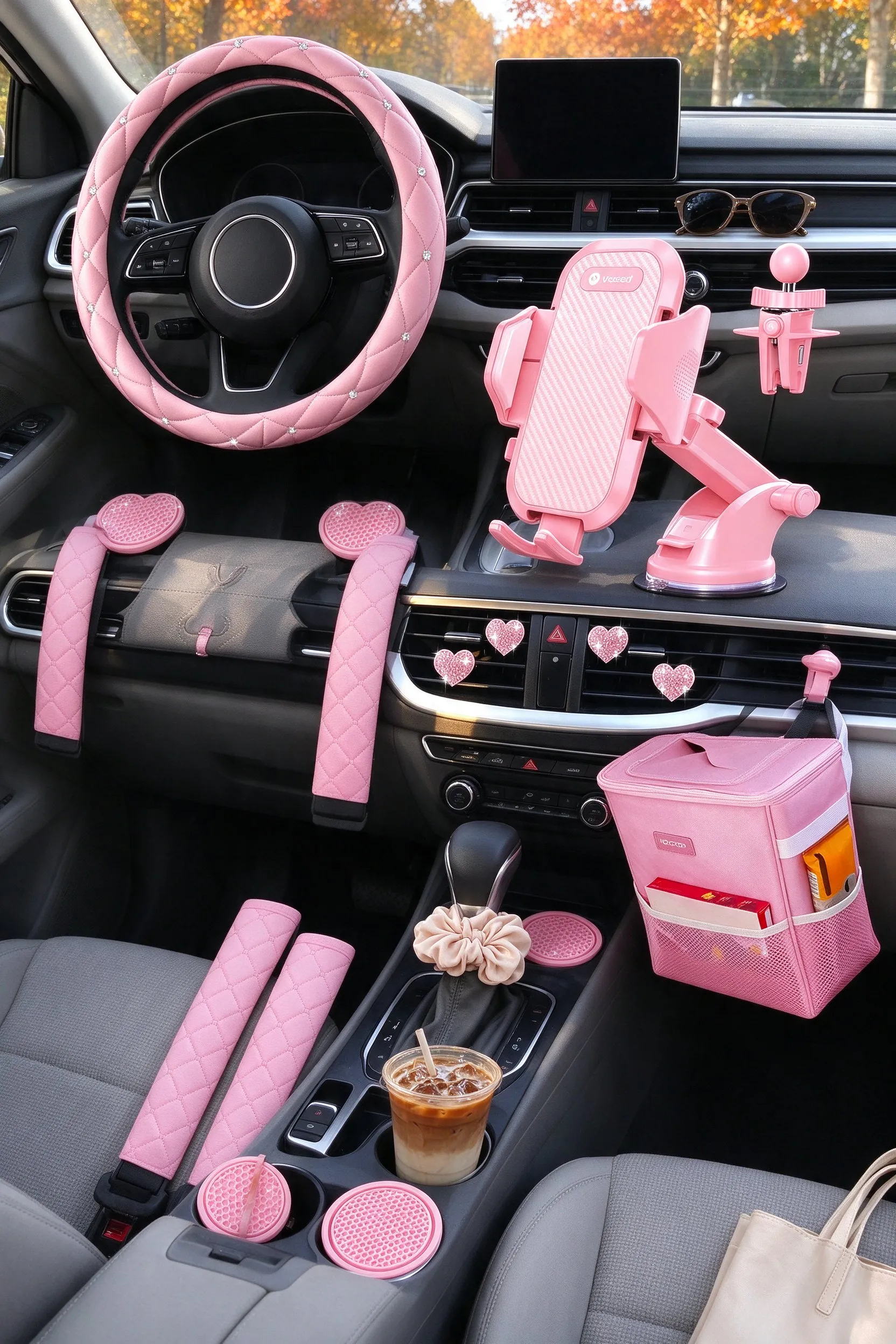 Styled scene: car interior decked out with every pink accessory installed: rhinestone steering wheel cover on the wheel, seat belt covers on the belts, coasters in the cup holders, heart vent clips on the vents, phone holder on the dash, trash can hanging behind the console.
